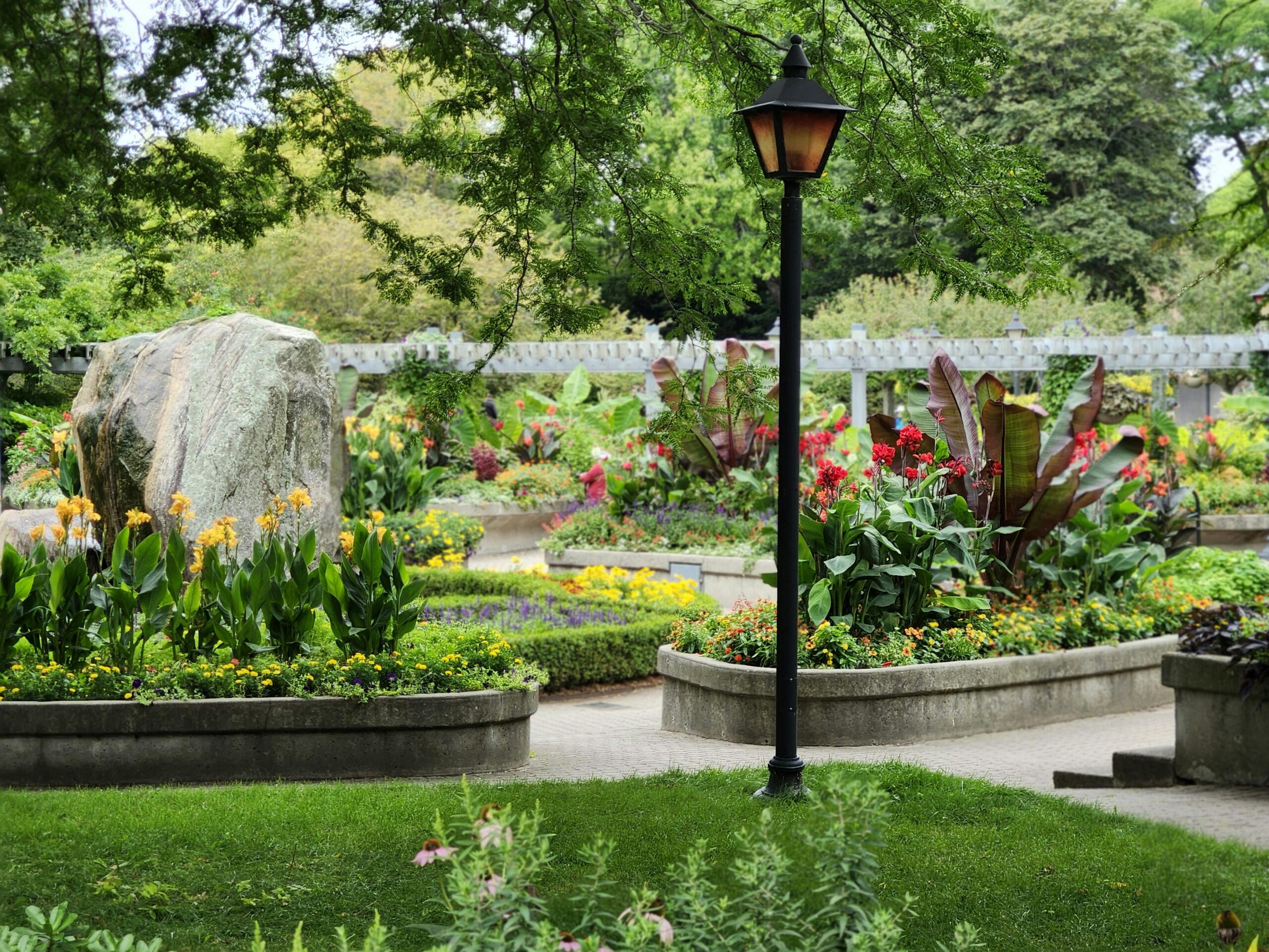 Lush floral garden with colorful blooms and a vintage lamppost in Toronto park.